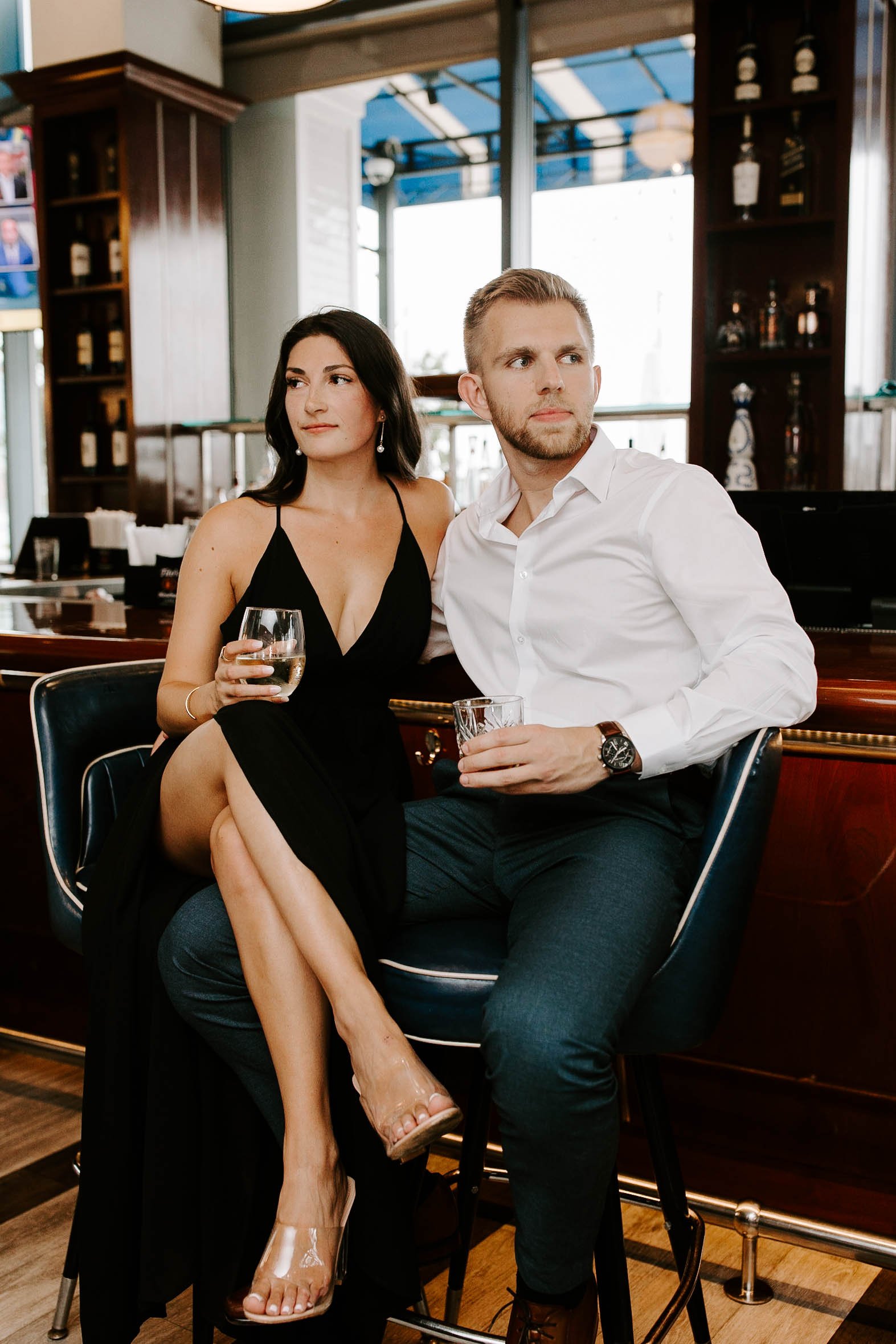  Engaged couple sitting at a bar holding alcoholic drinks 