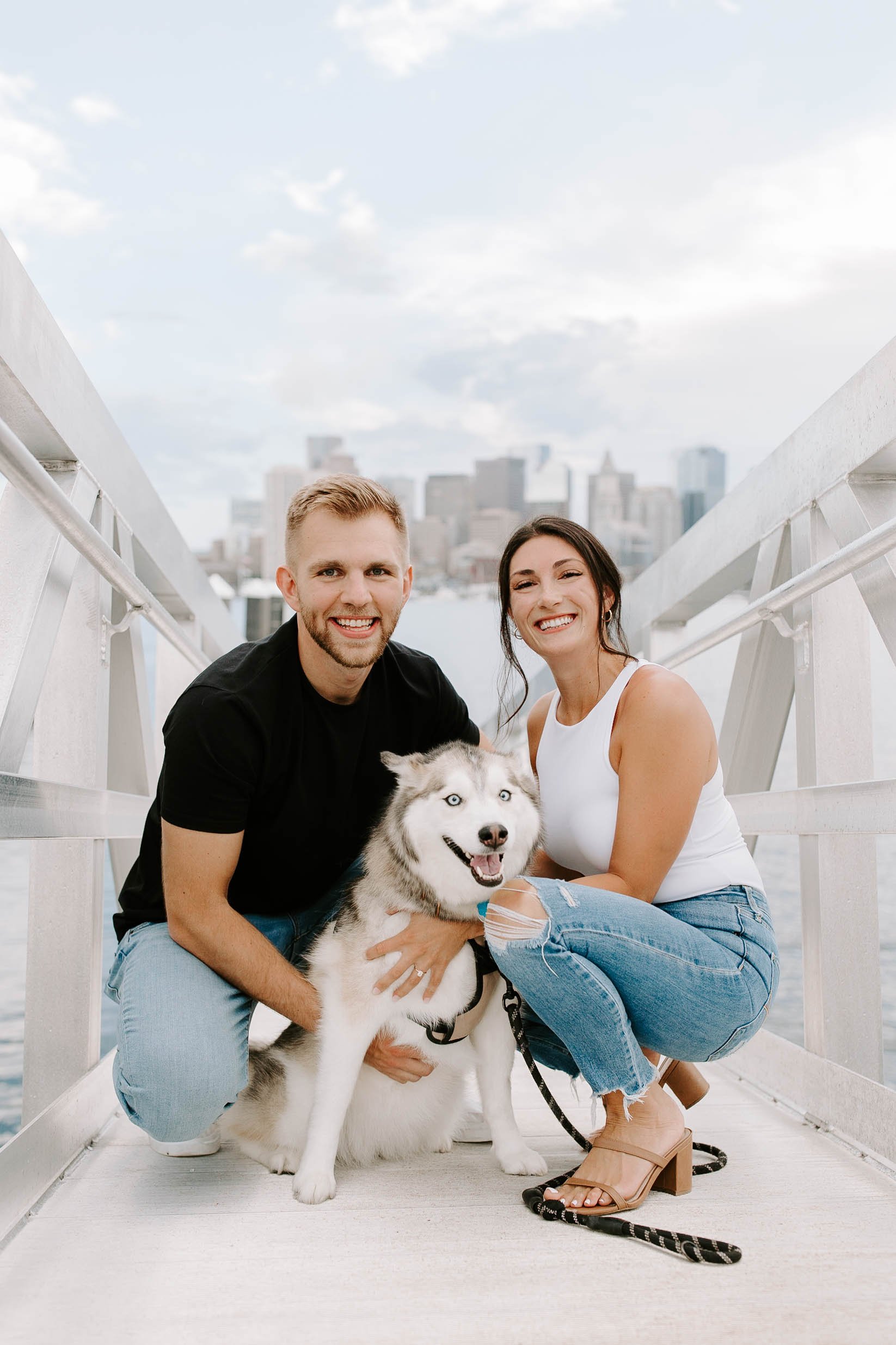  Engaged couple smiling holding their husky at seaport in Boston 