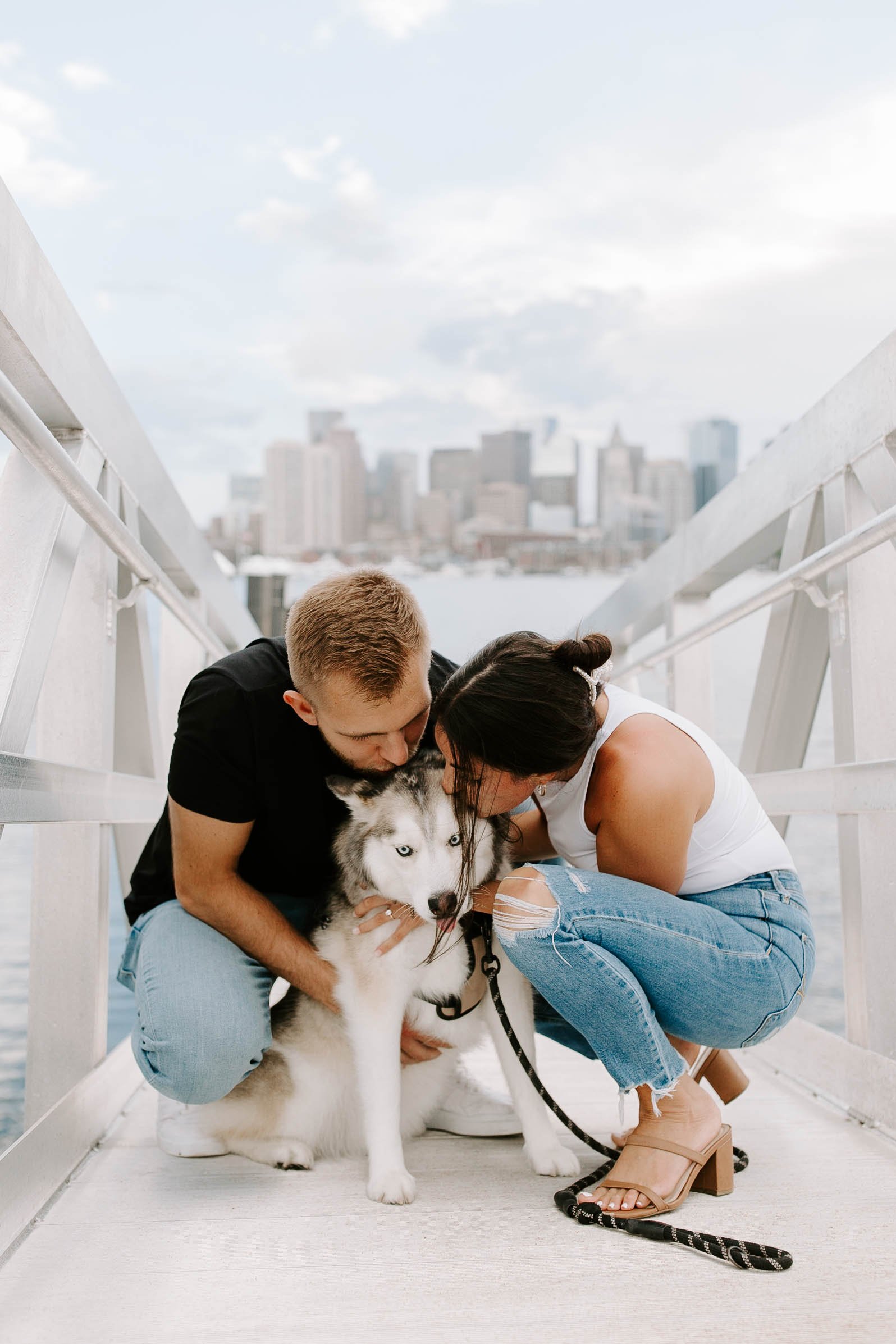  Engaged couple smiling holding and kissing their husky at seaport in Boston 
