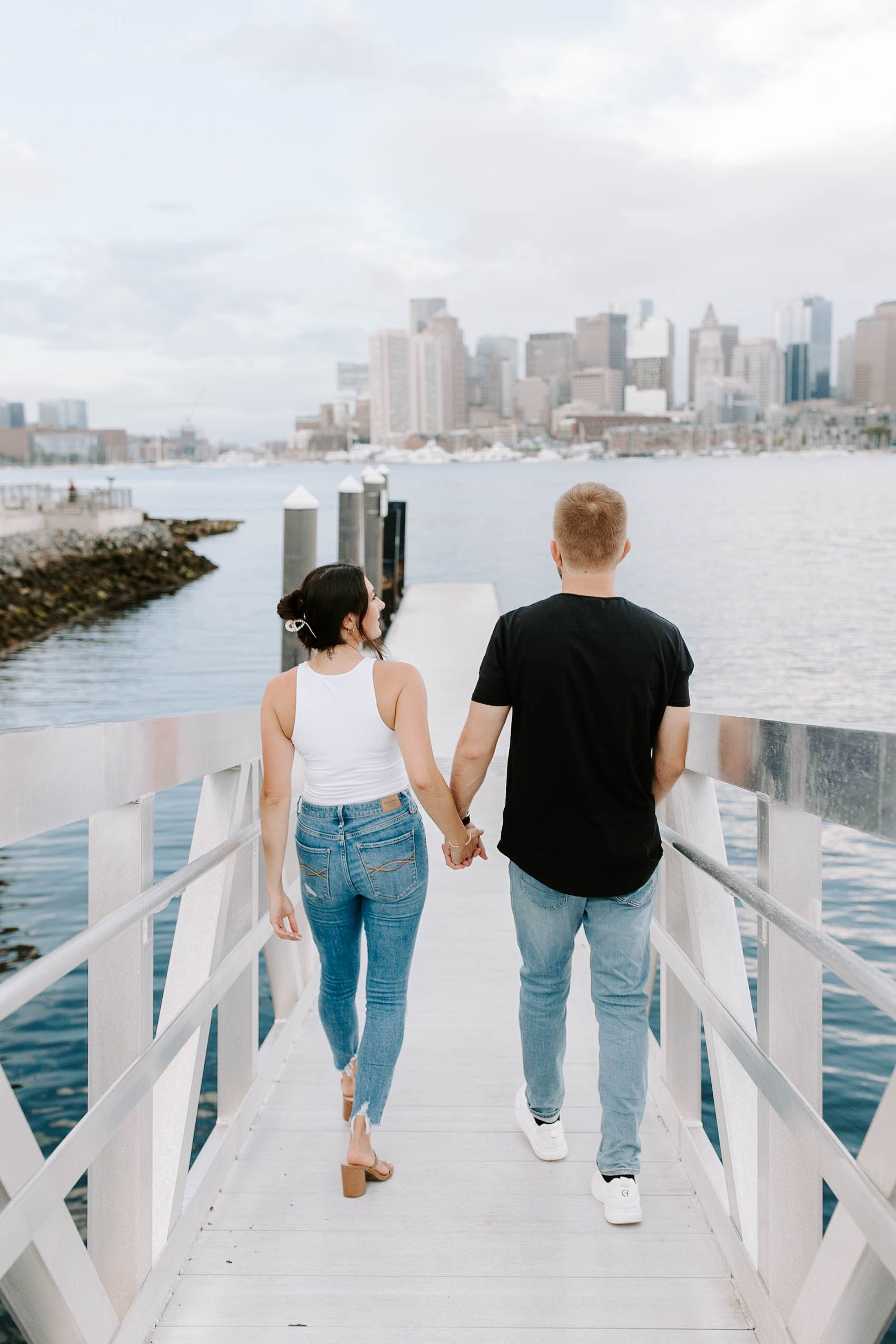  Engaged couple walking down the seaport with the skyline view in the background for their boston Seaport engagement session 