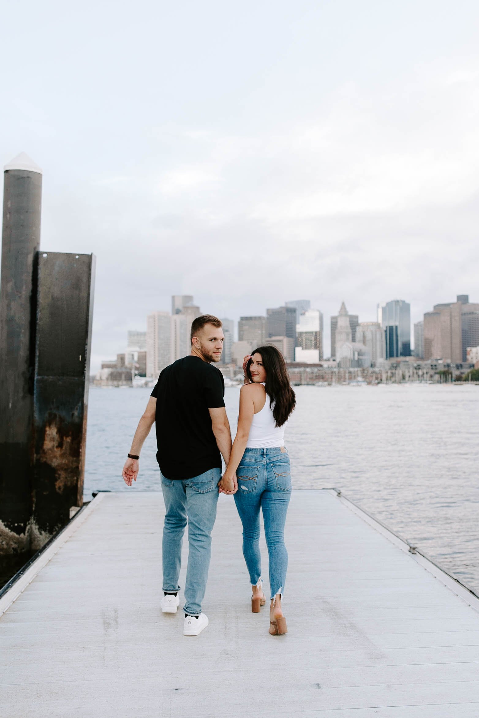  Engaged couple walking in front of skyline view  for their boston Seaport engagement session 
