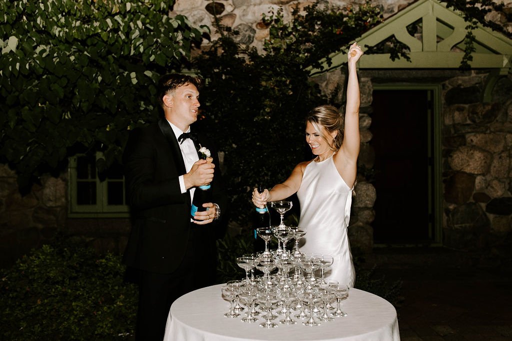 Bride and groom popping champagne to poor in champagne tower