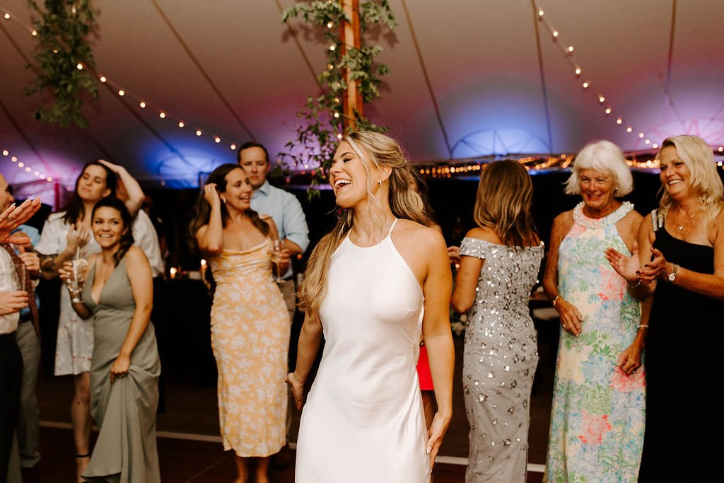 Bride smiling and dancing on wedding reception dance floor in a beautiful white slip dress