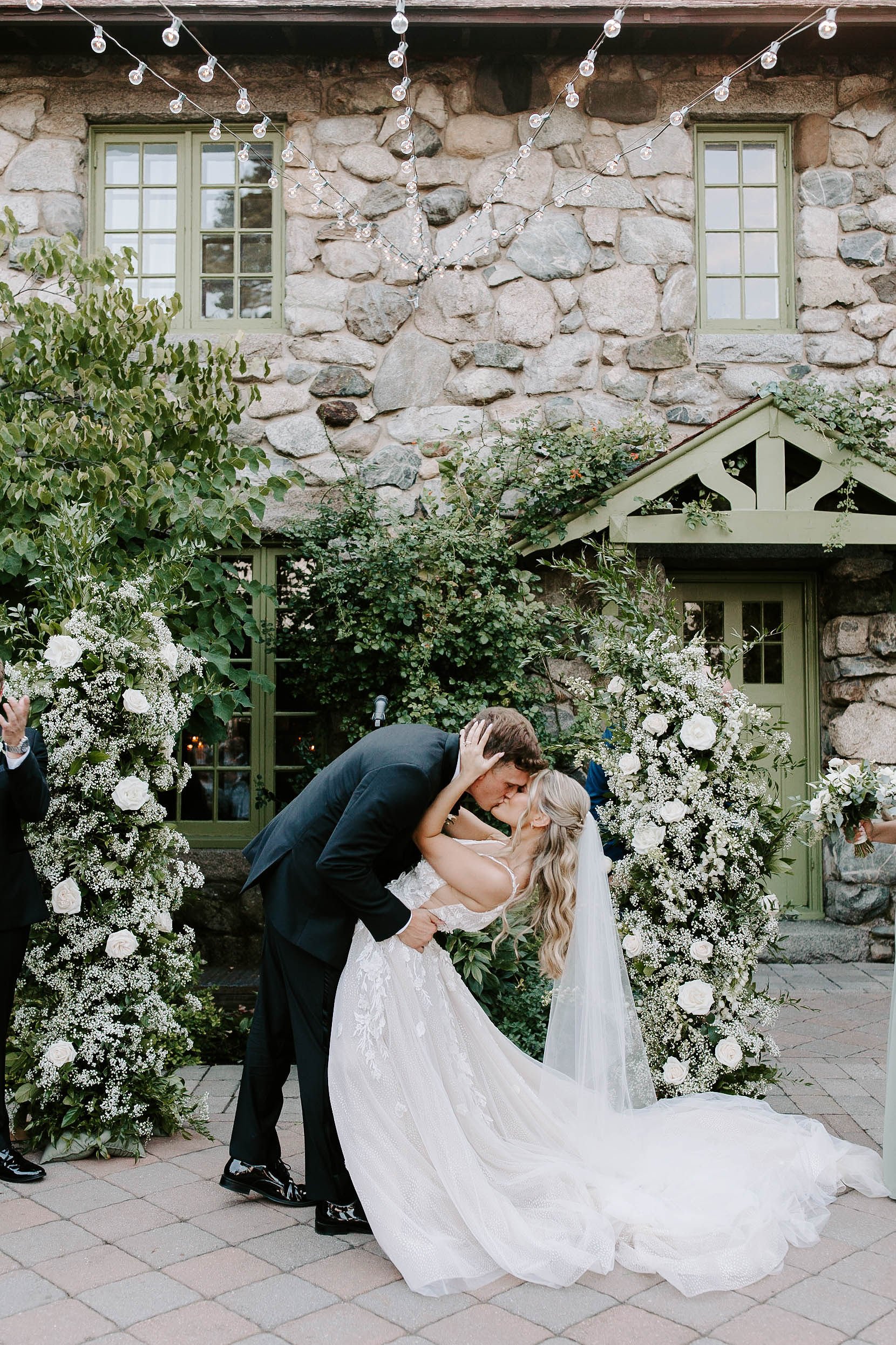 Bride and groom kissing after wedding ceremony in front of beautiful white and green floral arrangements