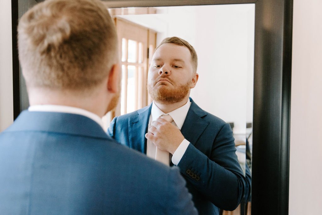 Groom getting ready in a blue tux and pink tie