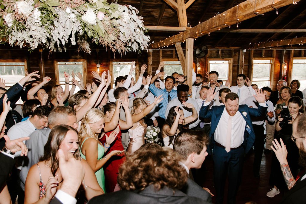 Bride, groom and guests dancing on wedding reception dance floor with their hands in the air