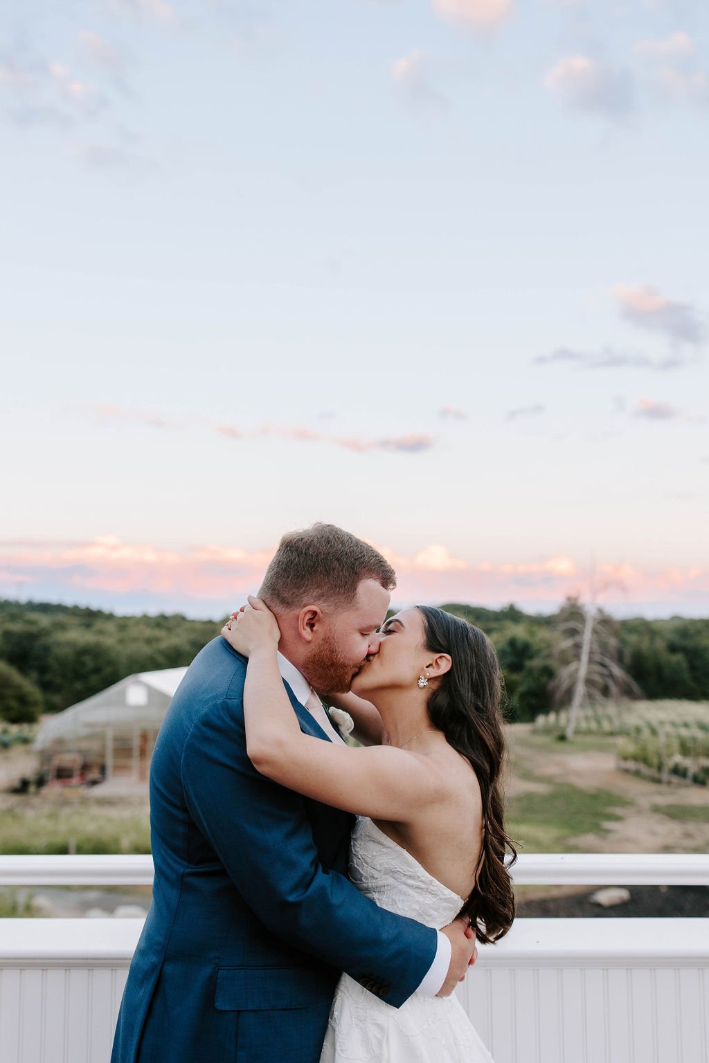 Bride and groom kissing on barn balcony during sunset