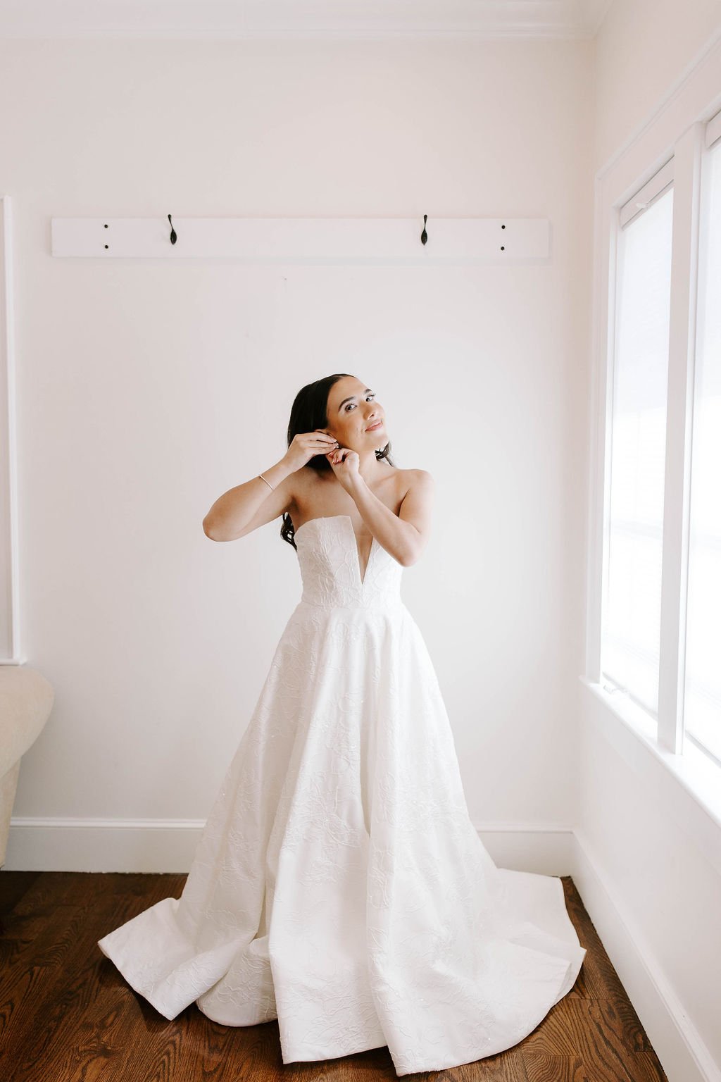 Bride wearing a strapless ball gown wedding dress putting in earrings  