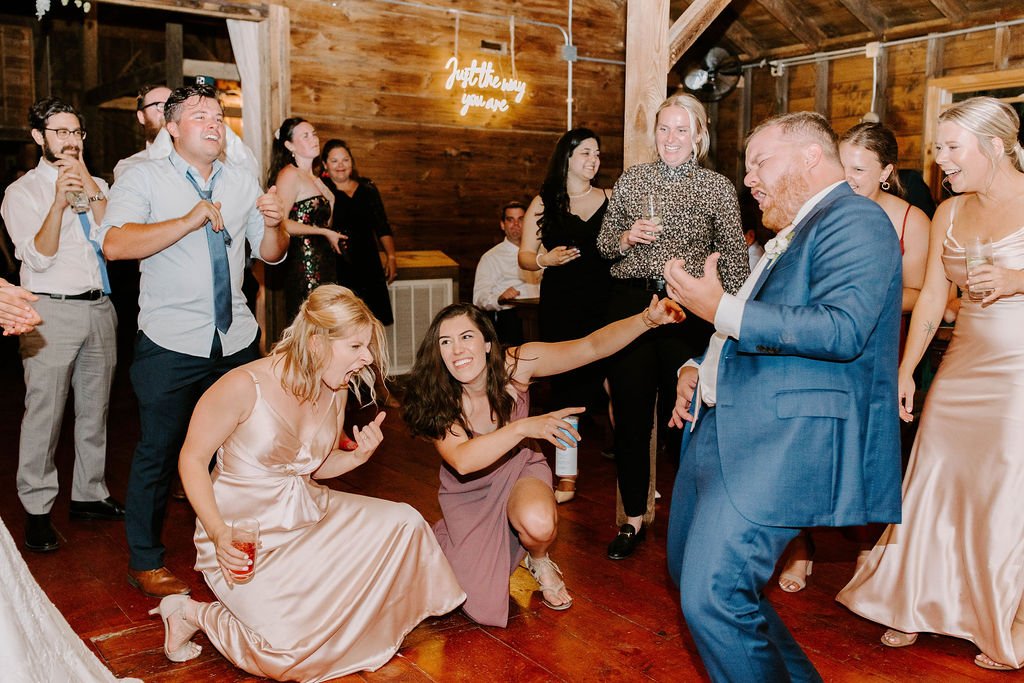 Groom playing air guitar dancing with wedding guests and bridesmaids