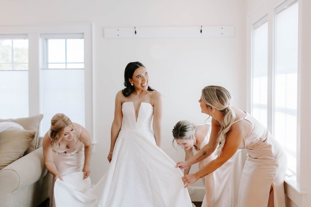 Bride smiling while her bridesmaids help her get ready for her rustic barn wedding
