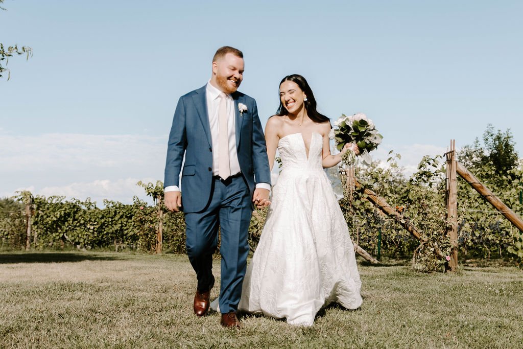 Bride and groom holding hands walking in a vineyard smiling and laughing