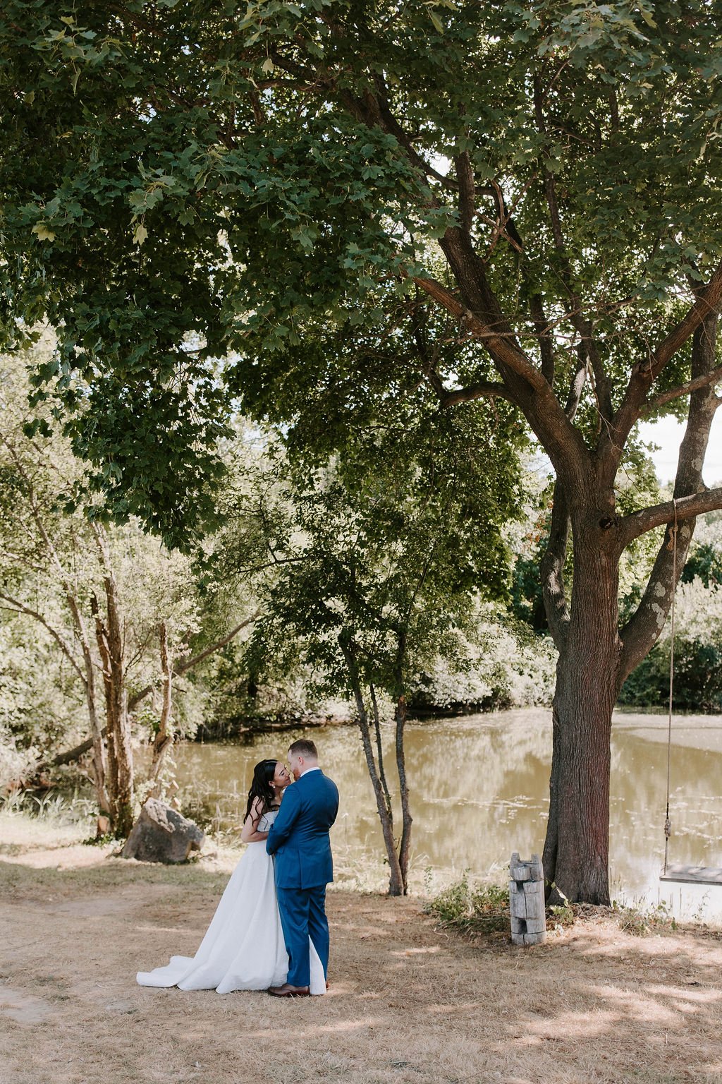 Bride and groom kissing standing under a tree on a farm