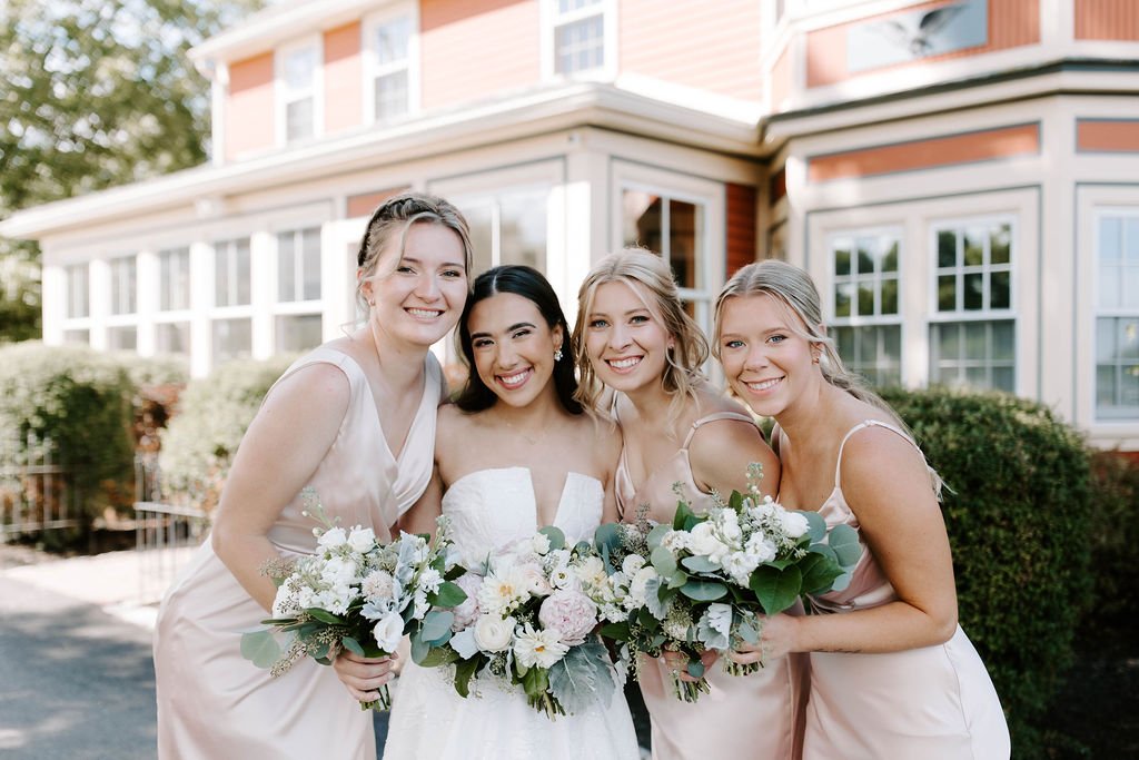 Bride smiling with her bridesmaids holing white and pink floral bouquets