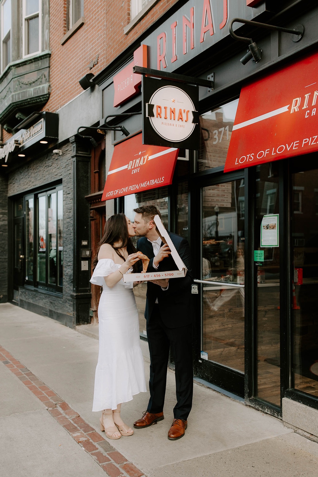 Man and woman kiss while holding pizza during North End engagement photos