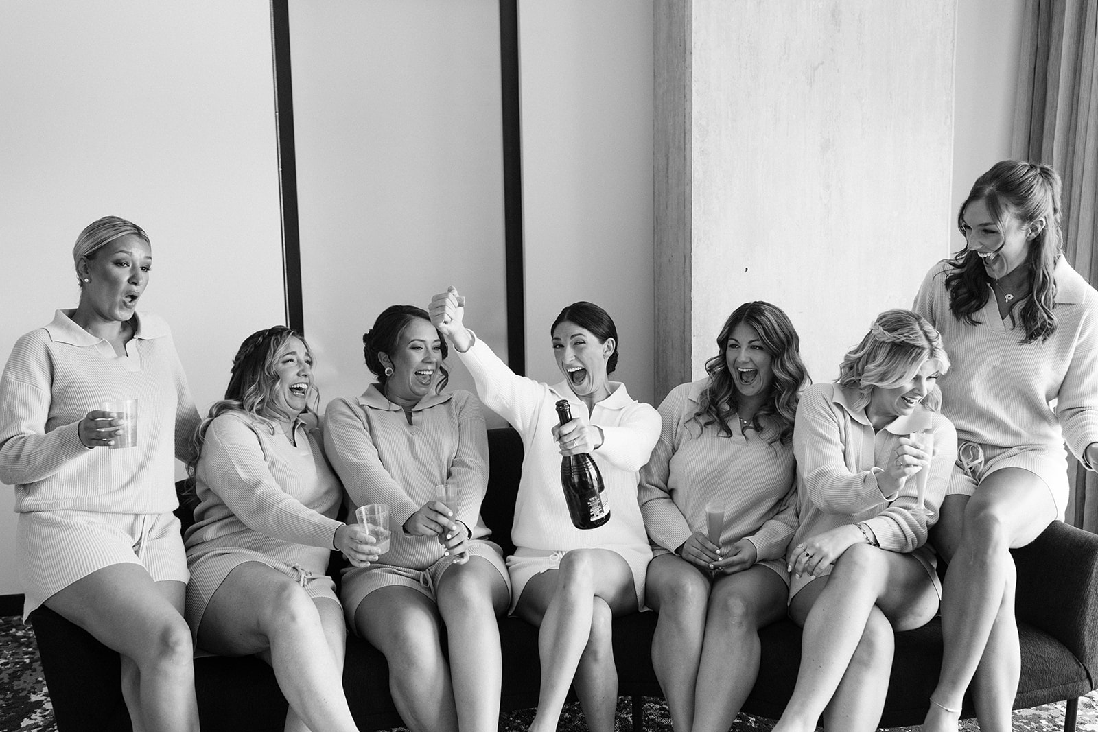Bridesmaids pose with the bride popping a bottle of champagne 