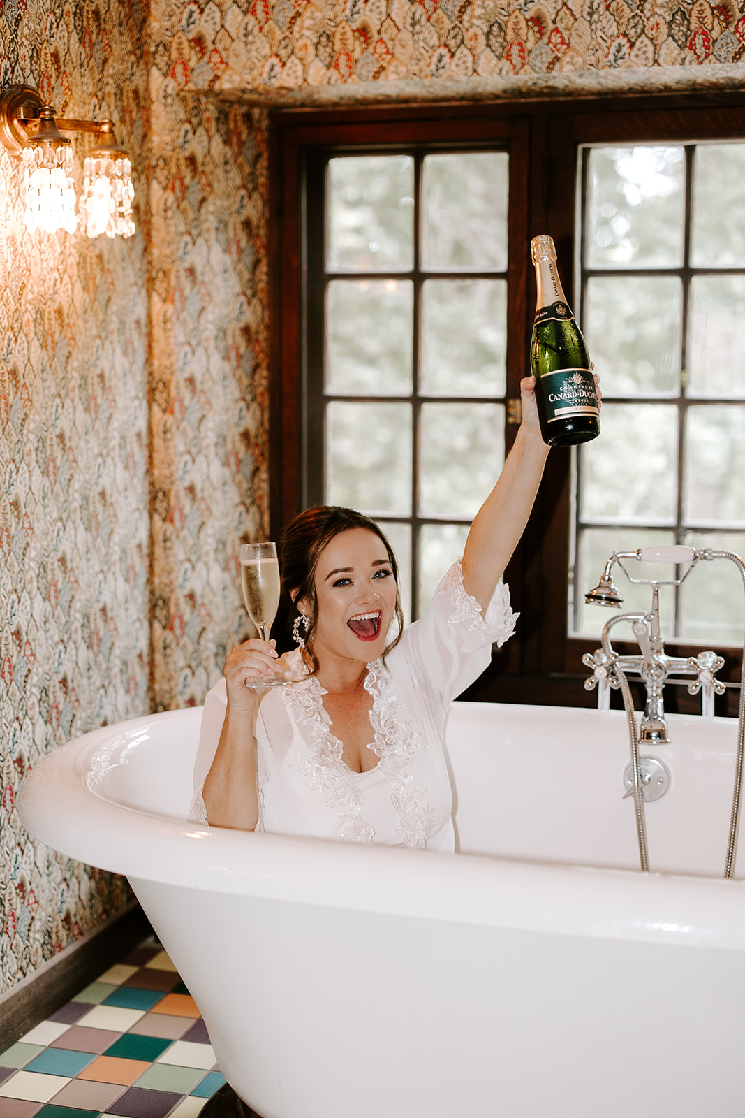 bride enjoys a glass of champagne in the bath tub as she prepares for her big day