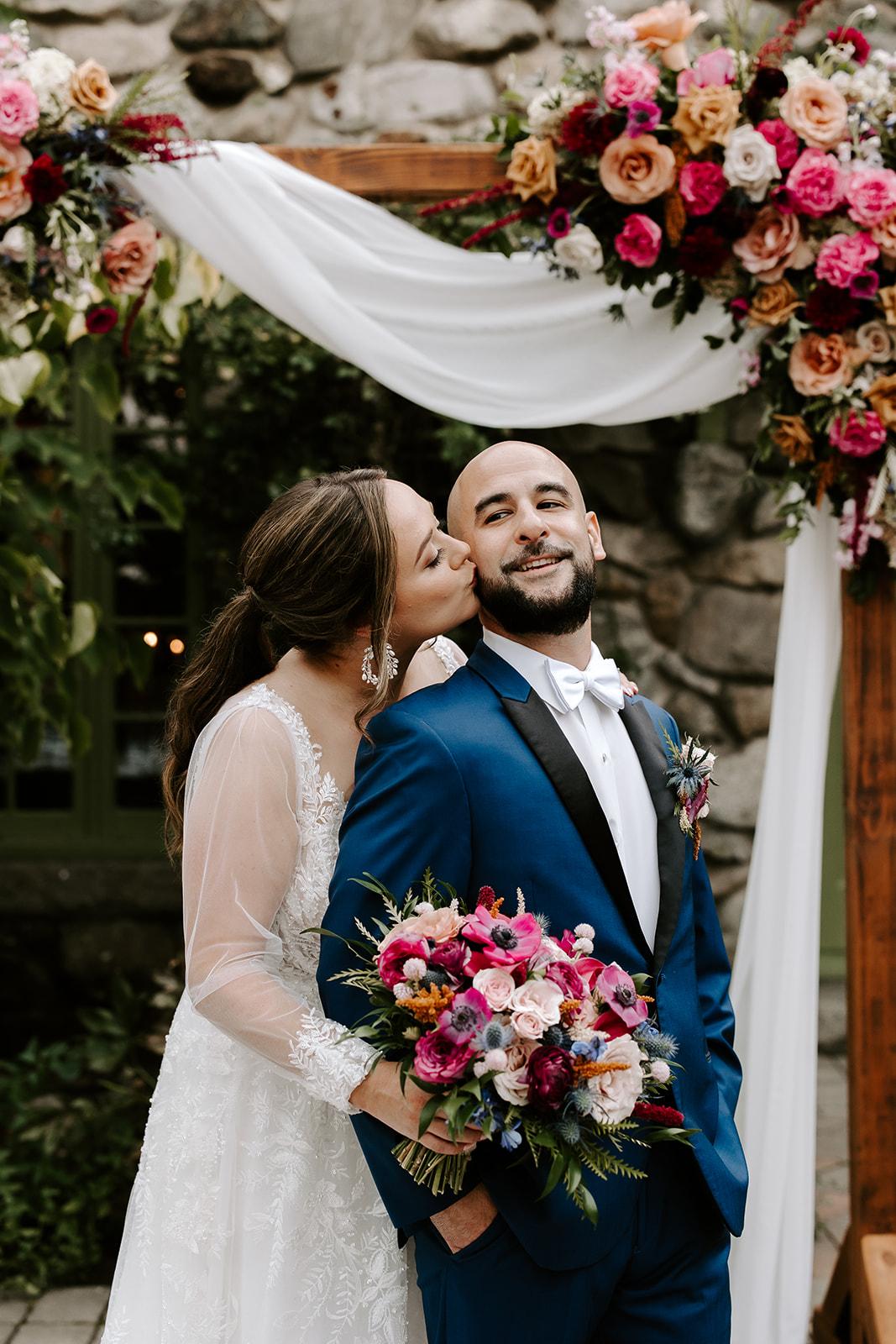 stunning bride and groom pose together under their wedding arch decorated with flavors