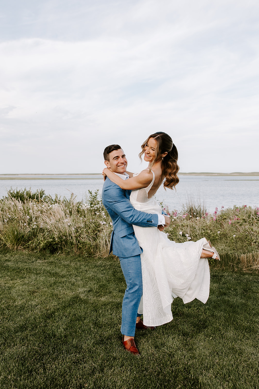 Newlyweds sharing a romantic sunset moment in a Cape Cod backyard, surrounded by glowing lanterns