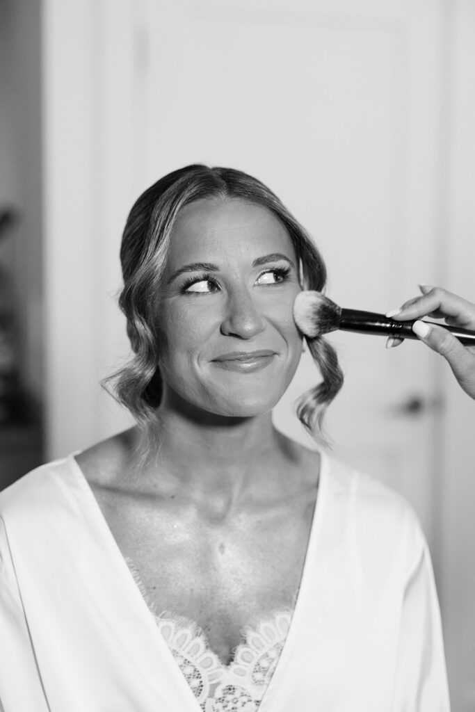 Bride smiling while getting her hair and makeup done by Erika Planer and Layza Souza for her backyard wedding in Orleans, MA