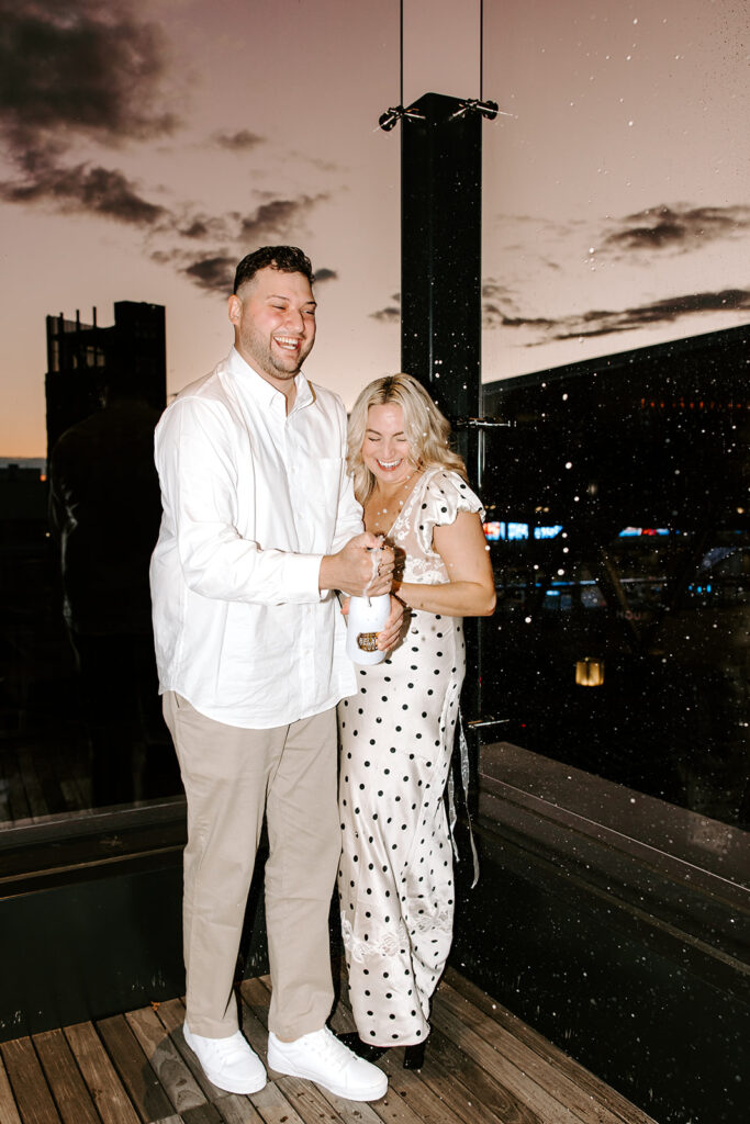 couple popping champagne with sunset behind them