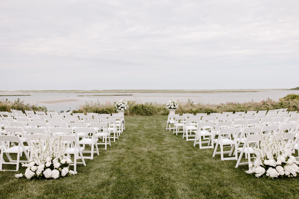 Backyard wedding ceremony setup in Orleans, MA, featuring rustic wooden chairs and lush greenery.
