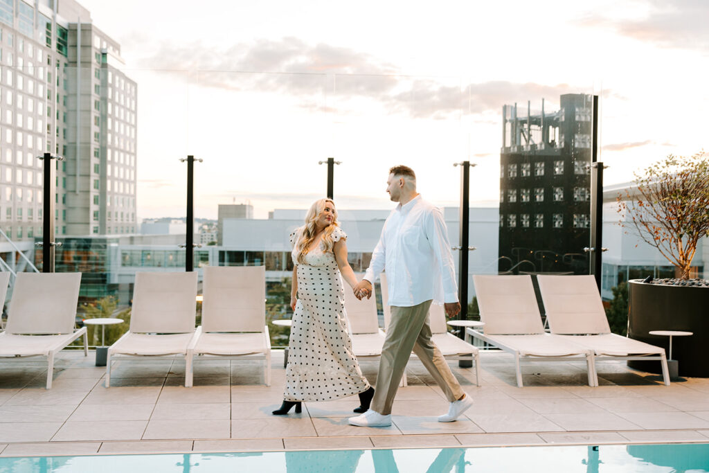 Engaged couple walking through the Omni Hotel Seaport hallway, laughing and holding hands.
