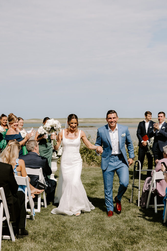 Newlyweds walking down the aisle as guests cheer and throw flower petals in celebration.