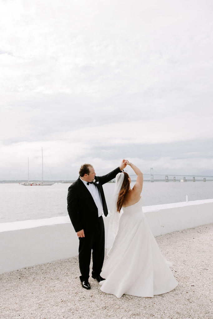Bride twirling in Anne Barge wedding dress along Newport’s rocky coast