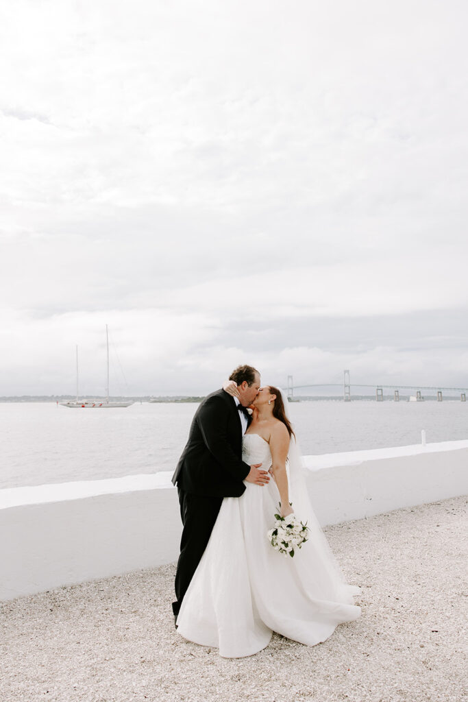 bride and groom kissing in front of newport bridge