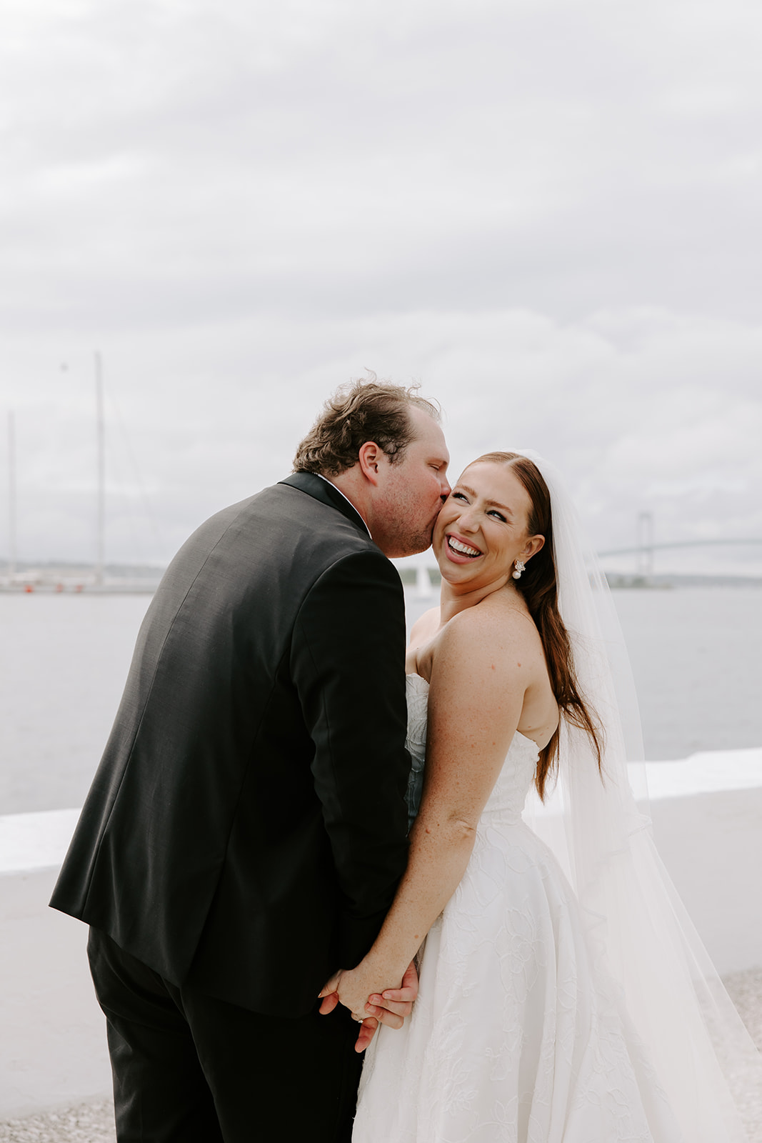 Elegant bridal portrait with wind blowing veil by the water