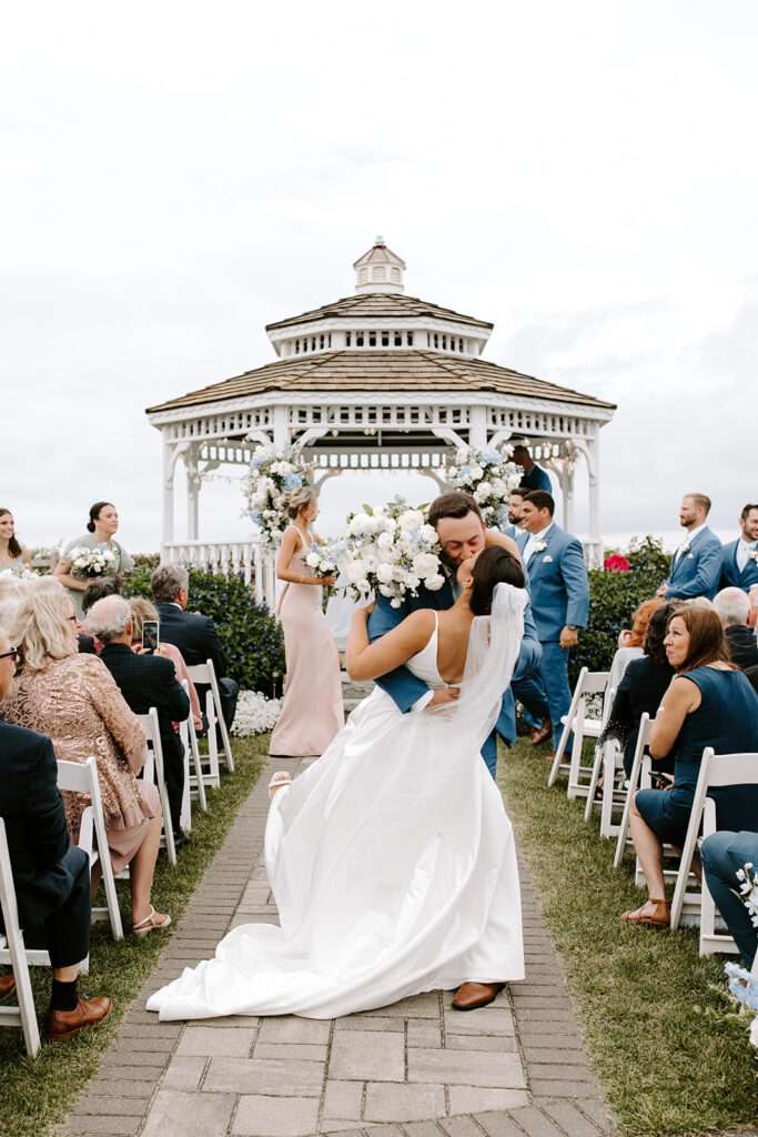 bride and groom kiss as they walk down the aisle