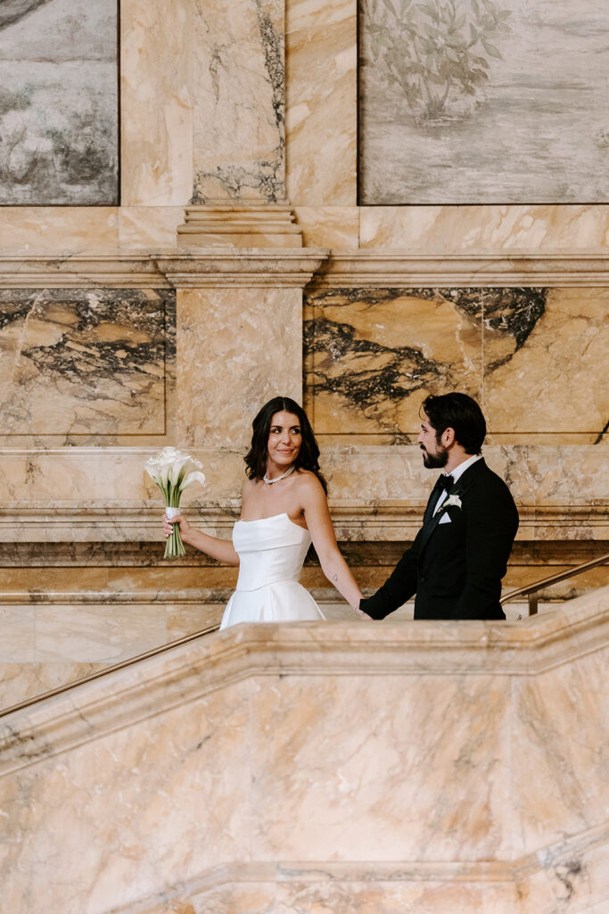 Candid photo of the bride and groom laughing together on the iconic stairwell of the Boston Public Library