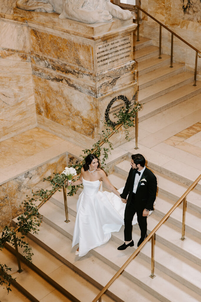 Candid photo of the bride and groom laughing together on the iconic stairwell of the Boston Public Library