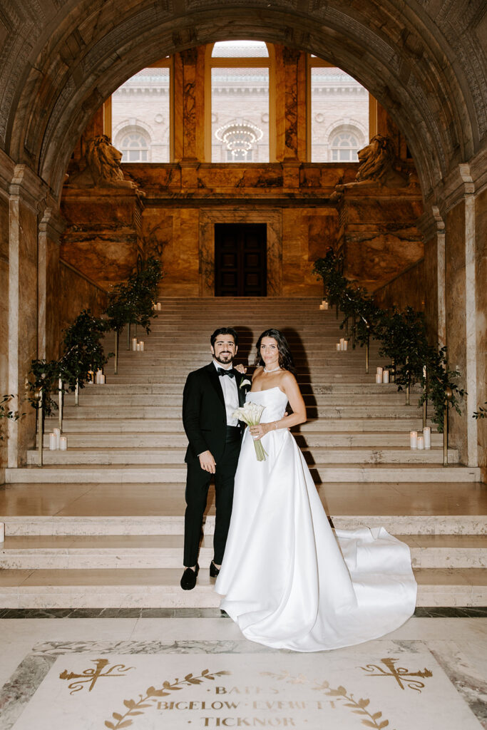 Black-tie wedding portrait of the newlyweds standing under the grand archway of the Boston Public Library