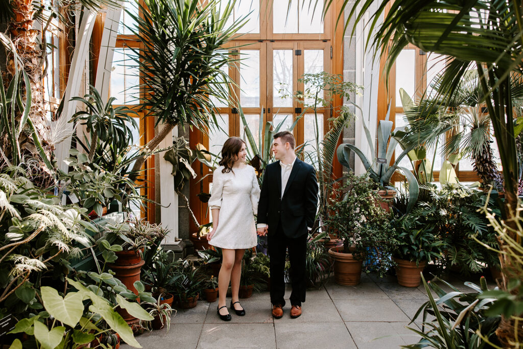Romantic engagement photo of couple standing under tropical greenhouse foliage