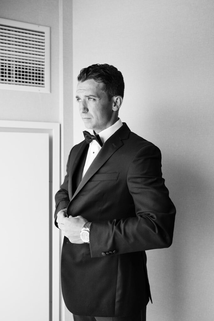 Groom adjusting cufflinks in hotel room at Patriot Place