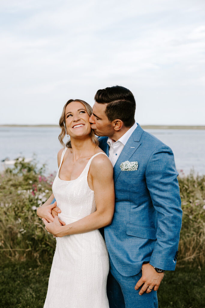 Groom kissing the bride’s forehead during golden hour wedding photos in a lush backyard setting