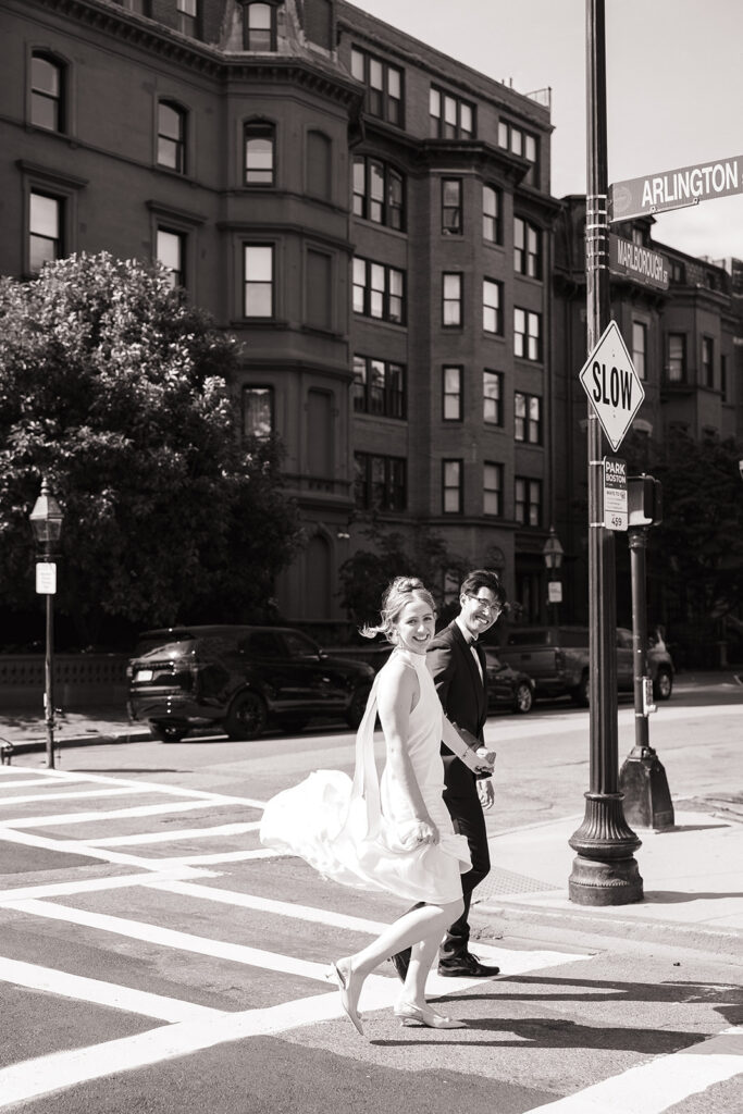 Bride and groom laughing while crossing a street in Boston's Back Bay neighborhood during their elopement