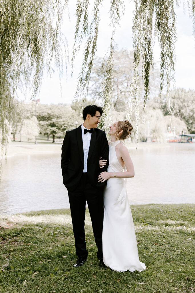Bride and groom smiling at each other by the Boston Public Garden pond with swan boats in the background