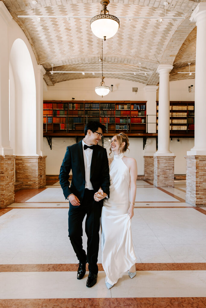 Bride and groom walking through the Boston Public Library Guastavino Room after their elopement ceremony, vaulted ceiling and colorful bookshelves behind them
