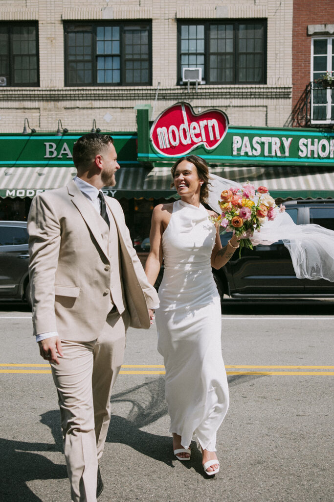 Bride and groom laughing together in front of Modern Pastry Shop in Boston's North End after their City Hall wedding, photographed by Genevieve Photography