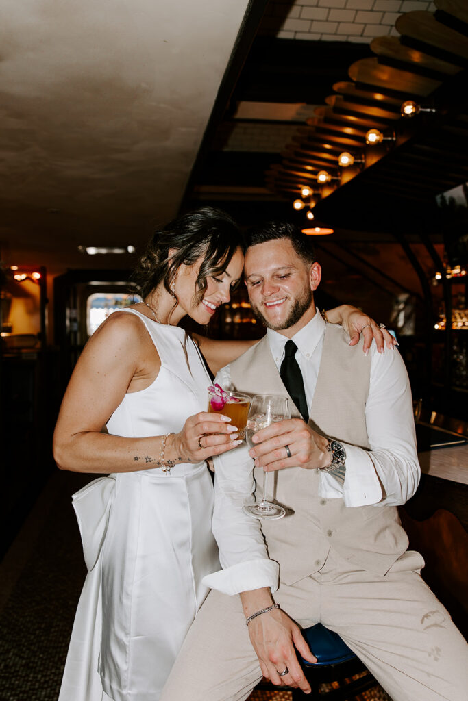 Bride and groom celebrating with cocktails at a Boston bar after their intimate City Hall wedding, bride in short white bow back reception dress, photographed by Boston wedding photographer Genevieve Photography