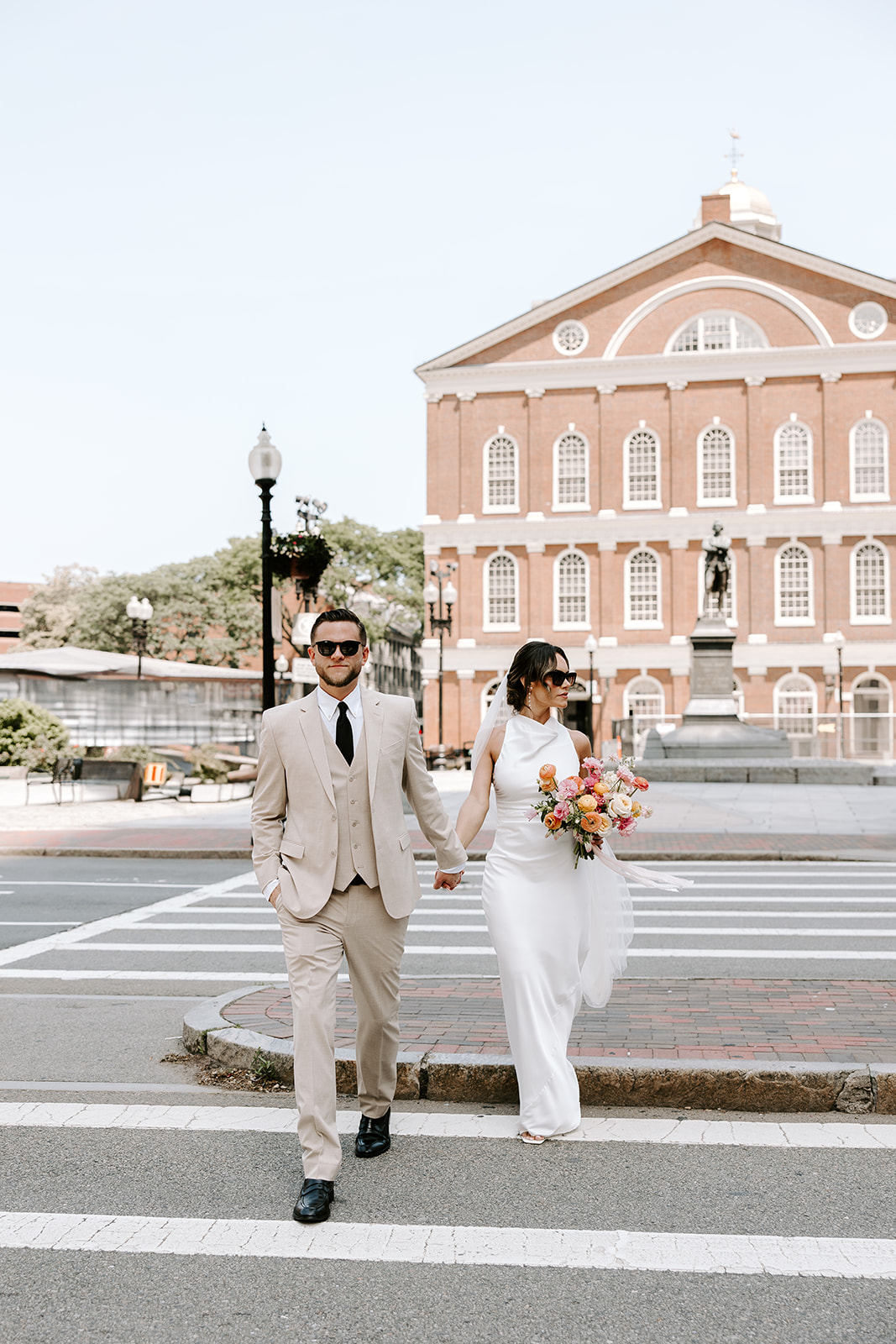 Boston City Hall wedding couple crossing the street in front of Faneuil Hall on their wedding day, bride in sleek white satin gown and groom in cream suit, photographed by Genevieve Photography