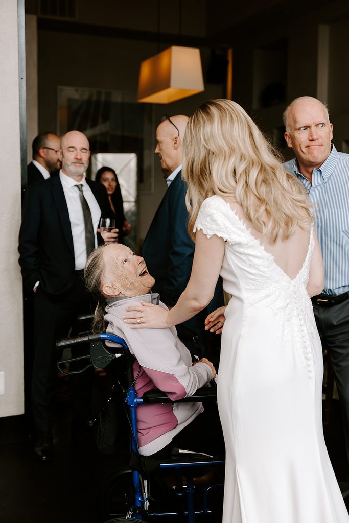 Bride in a lace back gown resting her hand on her grandmother's shoulder as her grandmother beams up at her during the reception at Mistral in Boston's South End, intimate restaurant wedding photographed by Boston elopement photographer Genevieve Photography
