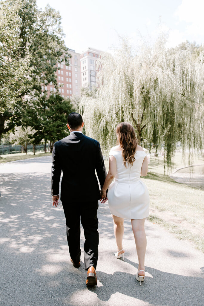 Bride and groom walking hand in hand along a shady path under the weeping willows in the Boston Public Garden after their Four Seasons Hotel Boston wedding, photographed by Boston elopement photographer Genevieve Photography